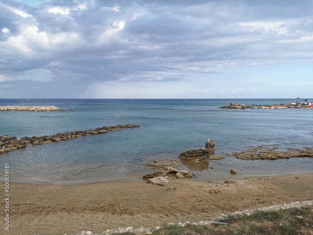 Bay of the Mediterranean Sea, sandy shore with a stone ridge and stones against a dramatic sky. Bay of the Mediterranean Sea, sandy shore with a stone ridge and stones against a dramatic sky.