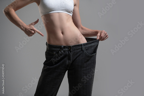 Dieting concept with oversized jeans. Skinny woman in too large jeans. Concept of successful weight loss. Thin girl in big trousers on a gray background. photo