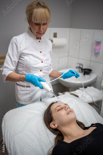 Beautician uses the darsonval device on the client's face. Professional skin care in the salon. The concept of cosmetology and rejuvenation.