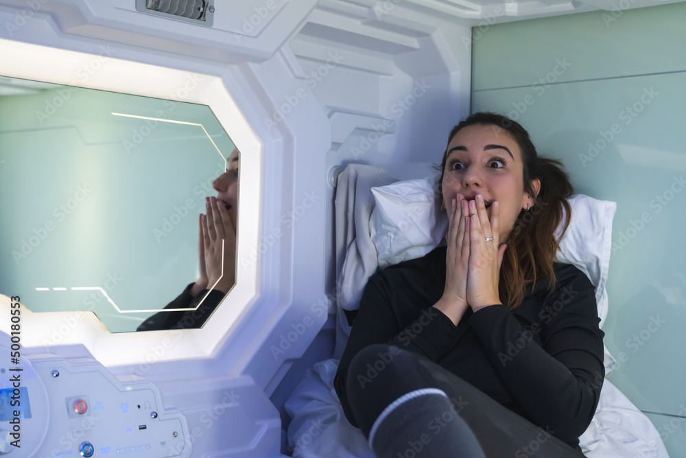 Brunette woman very surprised and worried about the news she sees on television in the capsule bedroom.