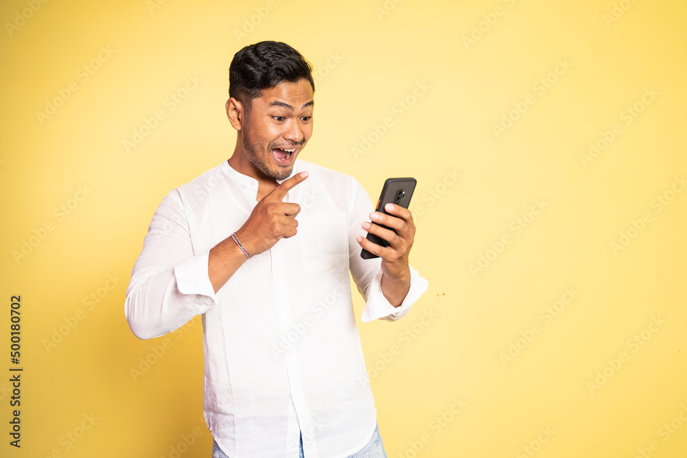 excited asian young man surprised when looking at the screen of a mobile phone on isolated background excited asian young man surprised when looking at the screen of a mobile phone on isolated background
