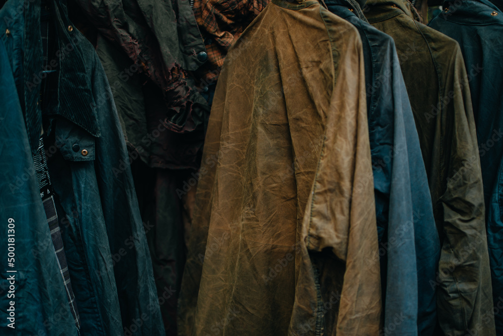 Fototapeta premium Hanger stand with vintage wax jackets. Secondhand brown jackets ,sweater and different Winter jackets. Men's wax jackets on hangers outdoors.