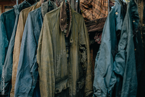 Hanger stand with vintage wax jackets. Secondhand brown jackets ,sweater and different Winter jackets. Men's wax jackets on hangers outdoors.