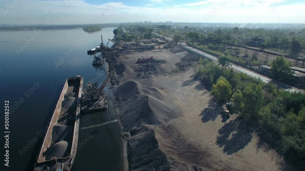 The moment of loading, port crane crushed stone on dry cargo ship. Loading of sand and crushed stone on the river in an industrial area. Orbit aerial panorama. The moment of loading, port crane crushed stone on dry cargo ship. Loading of sand and crushed stone on the river in an industrial area. Orbit aerial panorama.