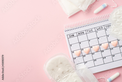 Top view photo of small pink hearts marks on the calendar sanitary napkins and tampons on isolated pastel pink background with copyspace
