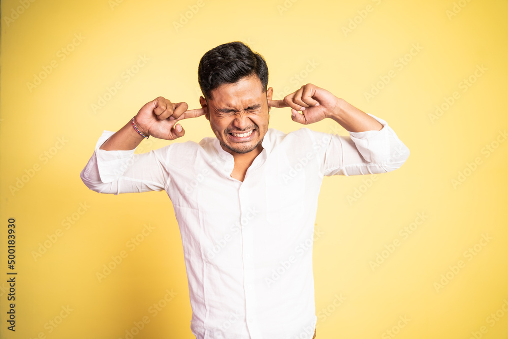 asian young man with uncomfortable expression with fingers covering ears on isolated background asian young man with uncomfortable expression with fingers covering ears on isolated background