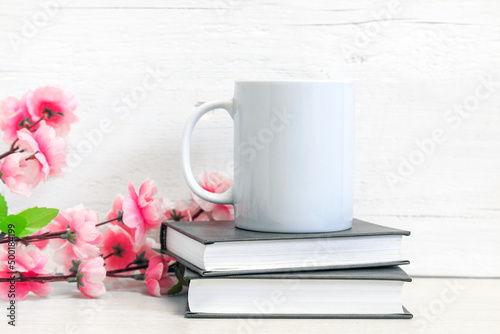 Mockup of a white ceramic mug on a table with books and flowers