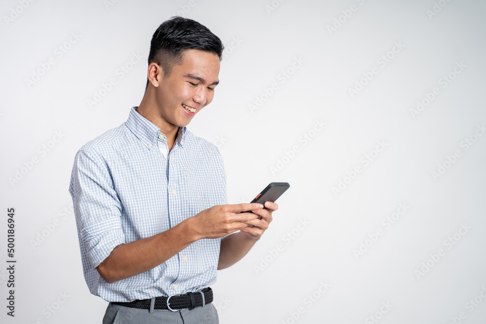 happy asian young man looking at the screen of a mobile phone on isolated background happy asian young man looking at the screen of a mobile phone on isolated background
