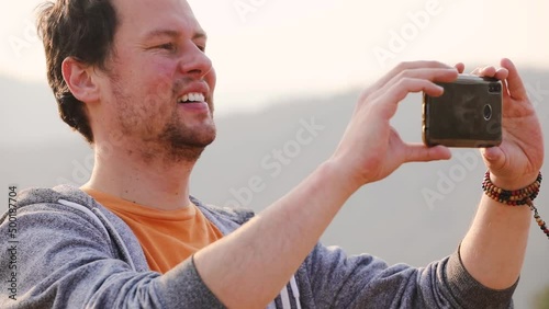 A caucasian male takes a photo with his phone on a hilltop on sunny afternoon