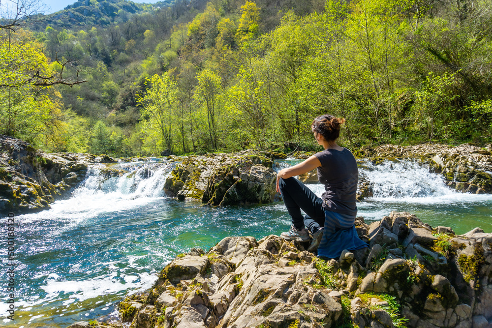 A young woman sitting on the Sella river between the Tornin a la Olla de San Vicente, near Cangas de Onis. Asturias. Spain
