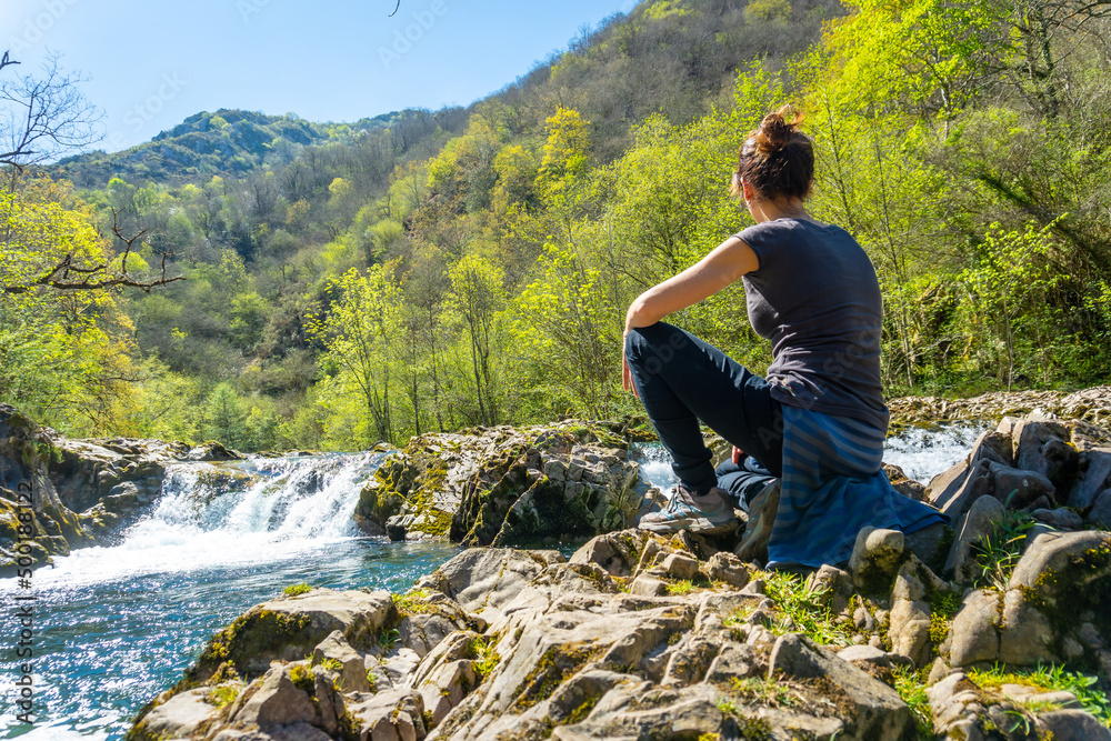 Naklejka premium A young woman sitting on the Sella river between the Tornin a la Olla de San Vicente, near Cangas de Onis. Asturias. Spain
