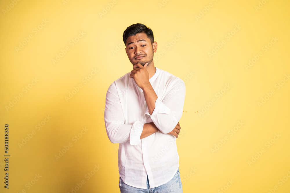 asian young man with sarcastic expression with hand holding chin on isolated background asian young man with sarcastic expression with hand holding chin on isolated background