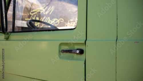 door handle in an old green car with graffiti on the glass