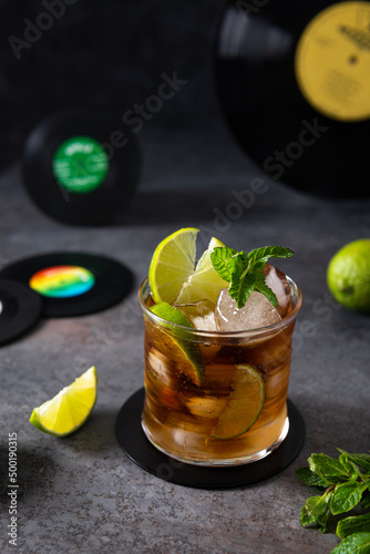 Canvas Print Fresh Cuba Libre cocktail with cola, lime and mint on dark background with vinil records
