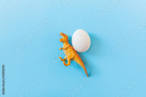Fototapeta Naklejka Na Ścianę i Meble -  Easter egg hunt holiday composition, white eggs with dinosaur on light blue backgroind. Seasonal spring kids game concept. Flat lay, top view, place for text, banner