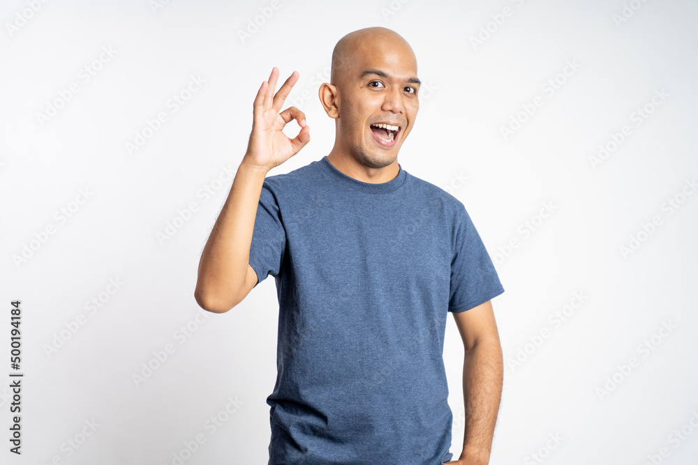 smiling asian bald man opening mouth with okay gesture while standing on isolated background smiling asian bald man opening mouth with okay gesture while standing on isolated background