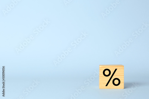 Wooden cube with percent symbol on light blue background. Space for text