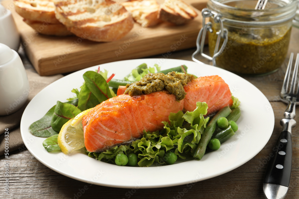 Tasty cooked salmon with pesto sauce and fresh salad served on wooden table, closeup Tasty cooked salmon with pesto sauce and fresh salad served on wooden table, closeup