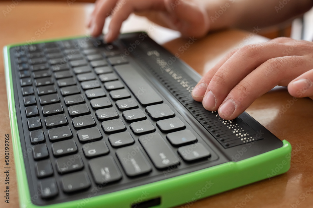 A blind man uses a computer with a Braille display and a computer keyboard. Inclusive device. A blind man uses a computer with a Braille display and a computer keyboard. Inclusive device.