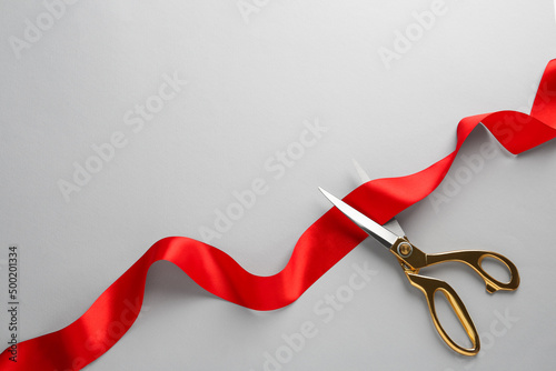 Red ribbon and scissors on light grey background, top view. Space for text