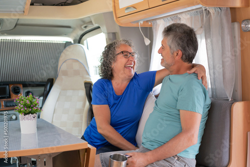 photo of a middle-aged retired couple sitting inside a motorhome. The couple laugh while looking at each other