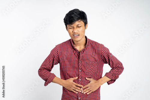 asian young man having stomachache holding his stomach with two hands on background isolated