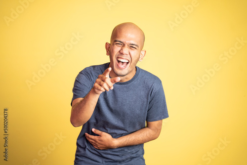 laughing young bald man with finger pointing on isolated background