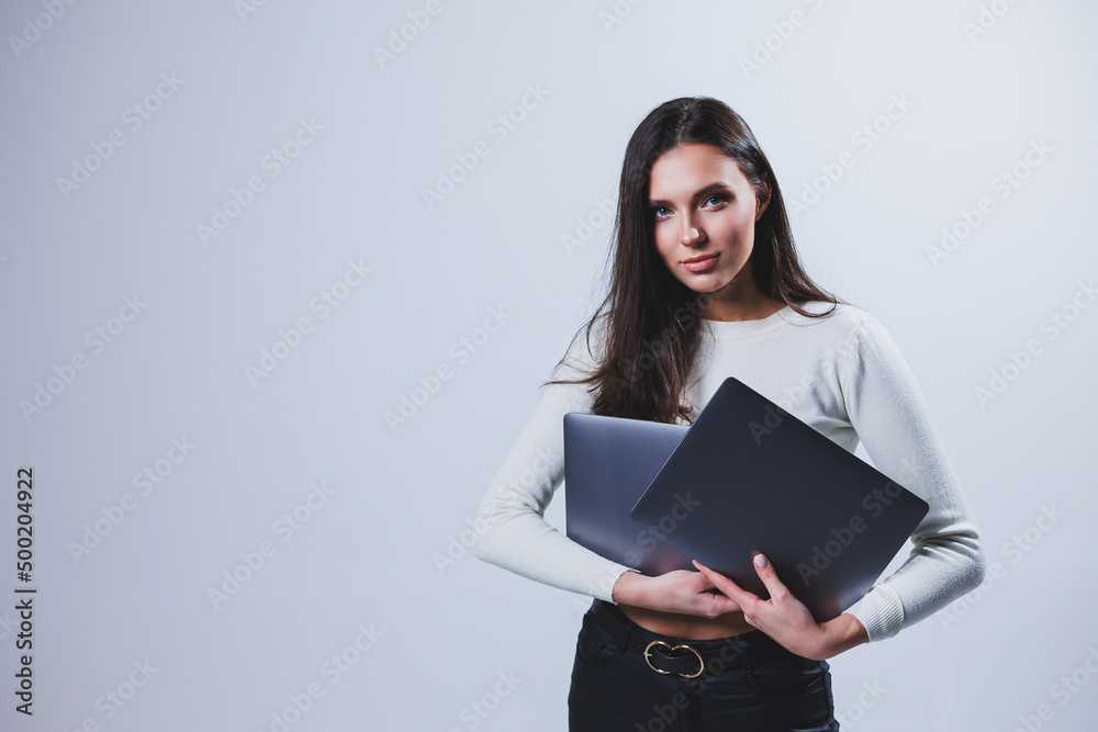 Young woman manager in a white shirt holds a portable laptop in her hands while standing on a gray background Young woman manager in a white shirt holds a portable laptop in her hands while standing on a gray background