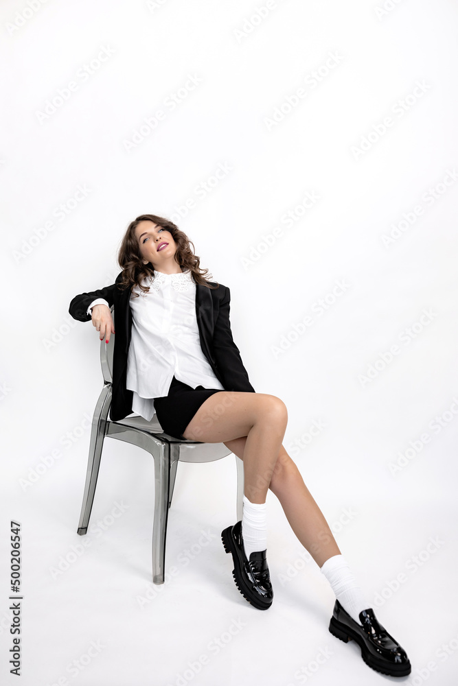 Elegant business woman posing in studio, looking at the camera, smiling. Beautiful young lady in stylish clothers sit on the chair, smiling. Pretty female shows success and self confidence. Elegant business woman posing in studio, looking at the camera, smiling. Beautiful young lady in stylish clothers sit on the chair, smiling. Pretty female shows success and self confidence.