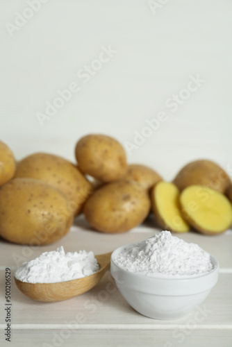 Starch and fresh raw potatoes on white wooden table. Space for text