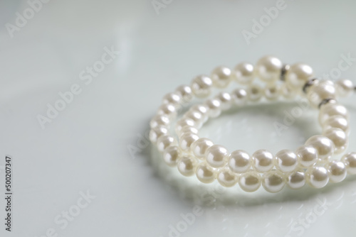 Elegant pearl necklace on white table, closeup. Space for text