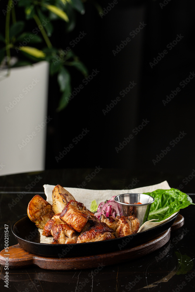 Grilled pork with baked golden potatoes served with red sauce on a dark background. Delicious Recipe. Pork Fillet Cooked