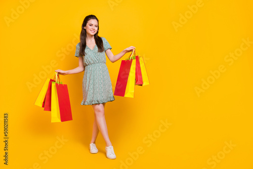 Photo of cute adorable lady dressed green dress walking holding shoppers empty space isolated yellow color background