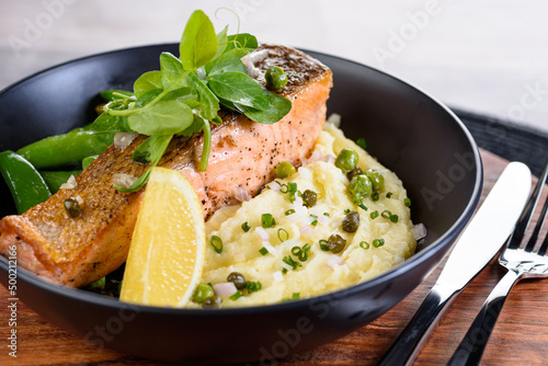 A serving of grilled salmon on a bed of mash potato and green beans.