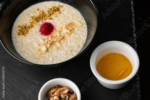 Semolina porridge for breakfast oat with nuts in black bowl served with honey isolated on black stone background. Homemade food. Tasty breakfast.