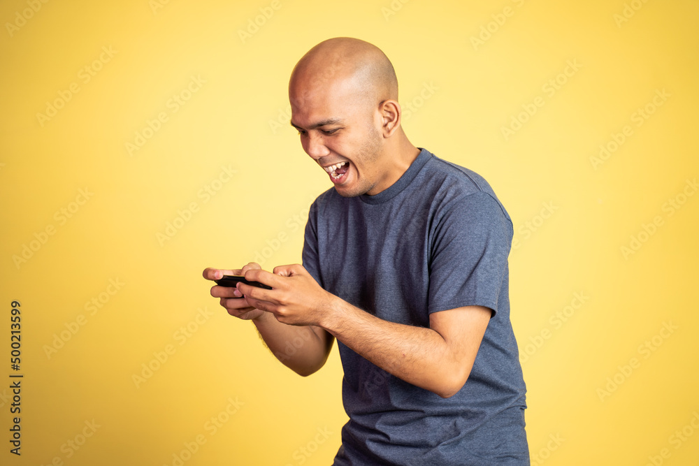 bald asian man laughing while playing game using smartphone on isolated background bald asian man laughing while playing game using smartphone on isolated background