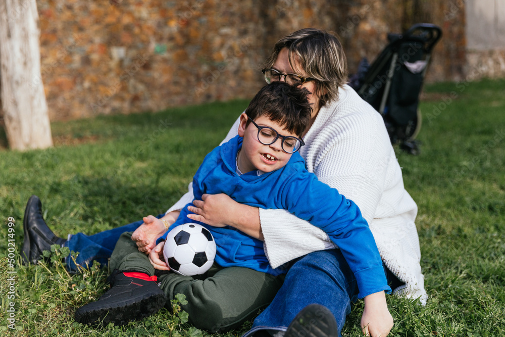 A mom playing with her son who has a disability holding a soccer ball in the park A mom playing with her son who has a disability holding a soccer ball in the park