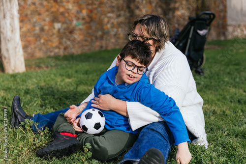 A mom playing with her son who has a disability holding a soccer ball in the park