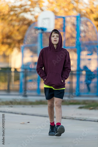 Front view of a young hooded boy walking away