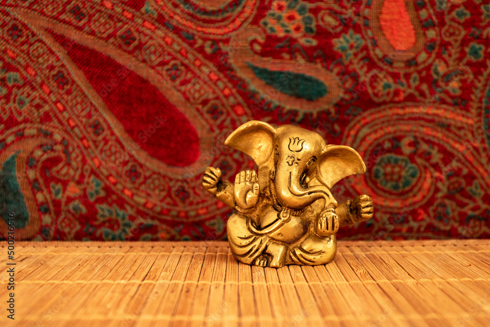 Golden ganesha statue on wooden mat with colorful background, closeup. Meditation and mindfulness concept Golden ganesha statue on wooden mat with colorful background, closeup. Meditation and mindfulness concept
