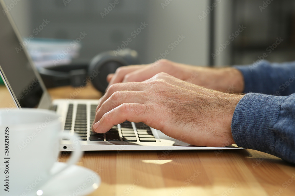 Fototapeta premium Man with laptop learning at wooden table indoors, closeup
