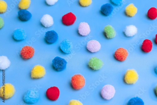Colorful pom-poms background, bright background, colorful pom-poms scattered in a chaotic manner on a blue background © Liiiz