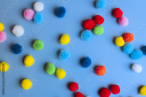 Colorful pom-poms background, bright background, colorful pom-poms scattered in a chaotic manner on a blue background