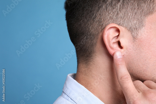 Man pointing at his ear on light blue background, closeup. Space for text
