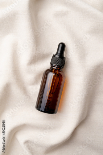 top view of amber glass essential oil droppper bottle with pipette on fabric wavy background