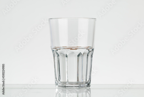 Faceted glass of water, half filled. Translucent glass on a white background.