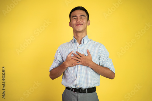 young man holding chest feeling relieve and comforting himself standing over white background photo