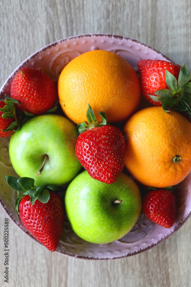 Pink bowl filled with fresh apples, oranges and strawberries on wooden table. Flat lay. Pink bowl filled with fresh apples, oranges and strawberries on wooden table. Flat lay.