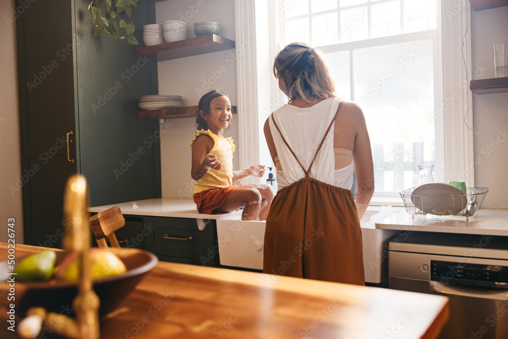 Single mother washing the dishes with her daughter at home Single mother washing the dishes with her daughter at home