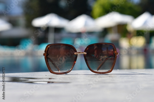Fototapeta Naklejka Na Ścianę i Meble -  Close up of sunglasses left at outdoor swimming pool. Selective focus.